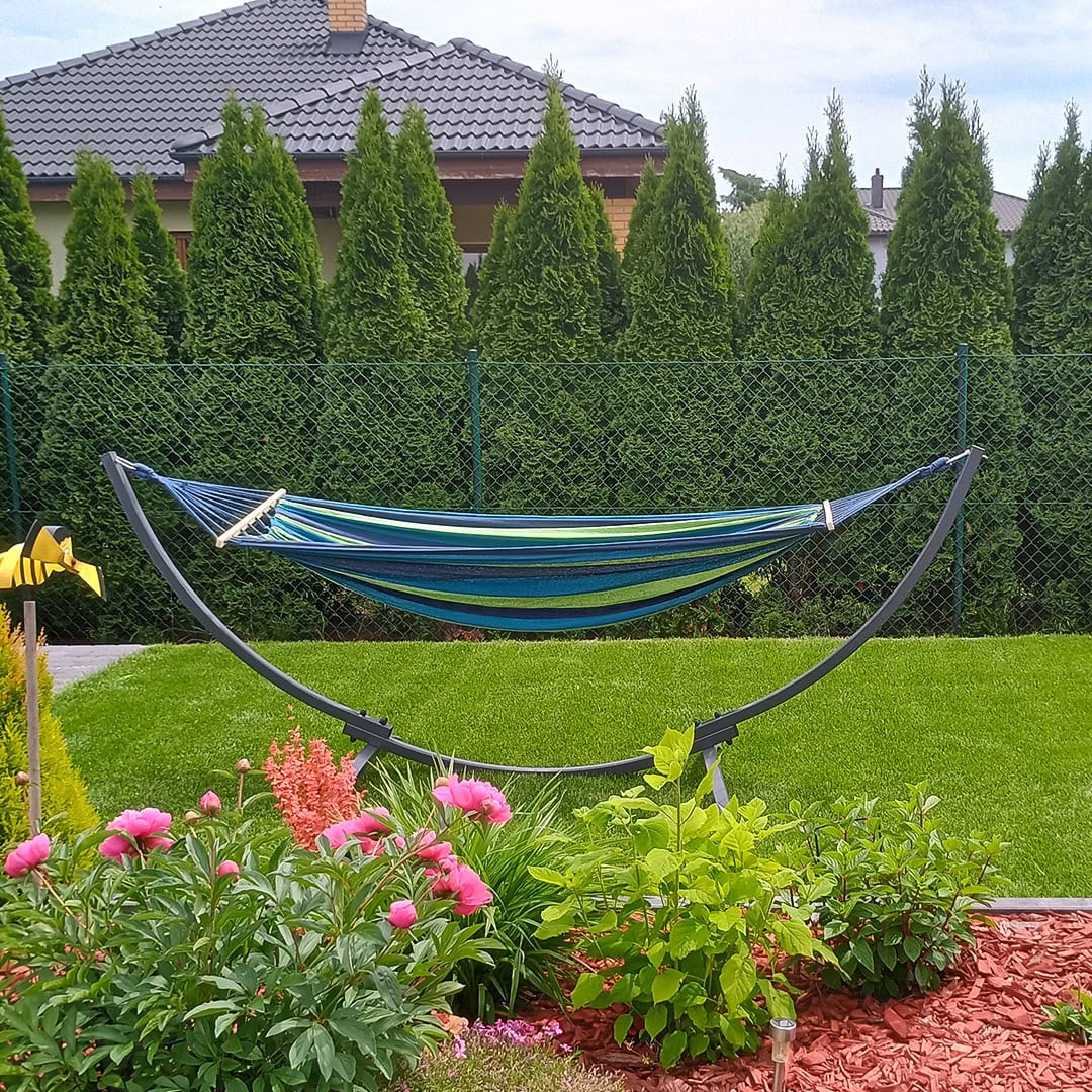Curved hammock stand with blue and green hammock in landscaped garden